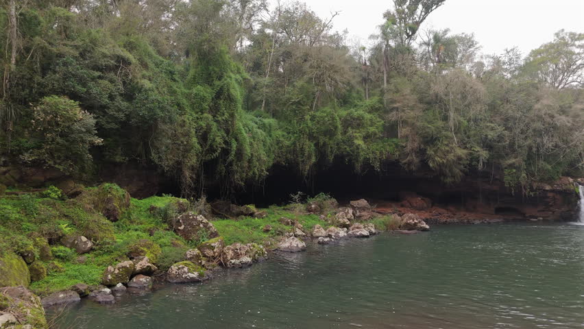Small waterfall flowing into serene pool surrounded by lush vegetation at Parque Natural Gruta India, Misiones, Argentina.