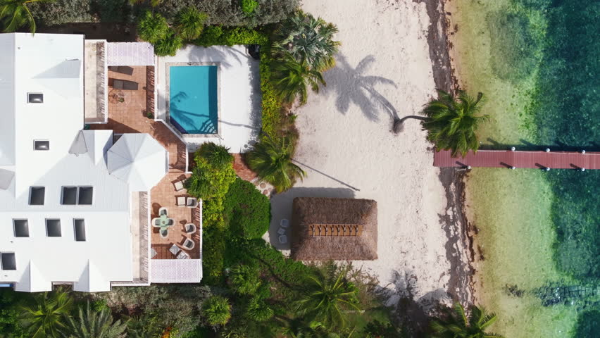 Experience breathtaking aerial views of a stunning beachfront property in Key West, Florida, featuring a luxurious pool, palm trees, and captivating turquoise oceans, perfect for relaxation