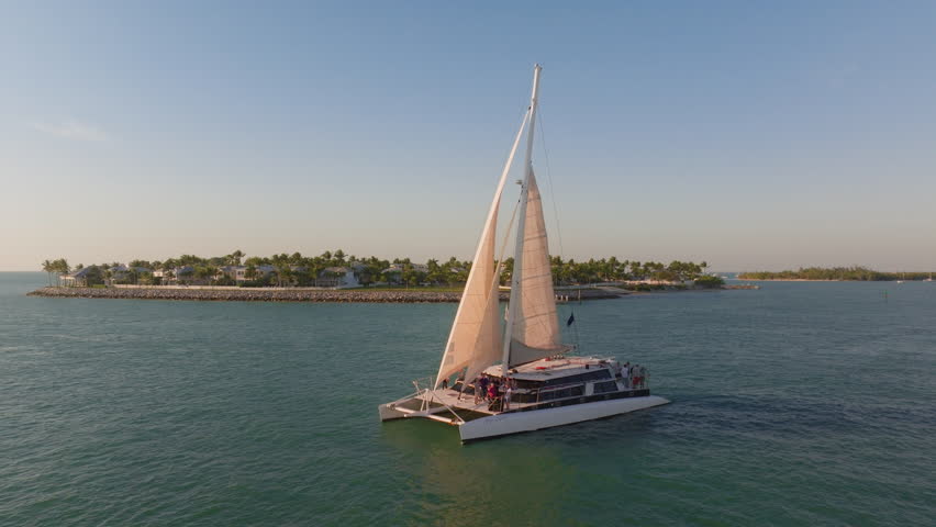 This stunning aerial photo showcases Sunset Key in Key West, with its clear blue waters and vibrant catamaran, set against a serene sunset backdrop that enhances its charm