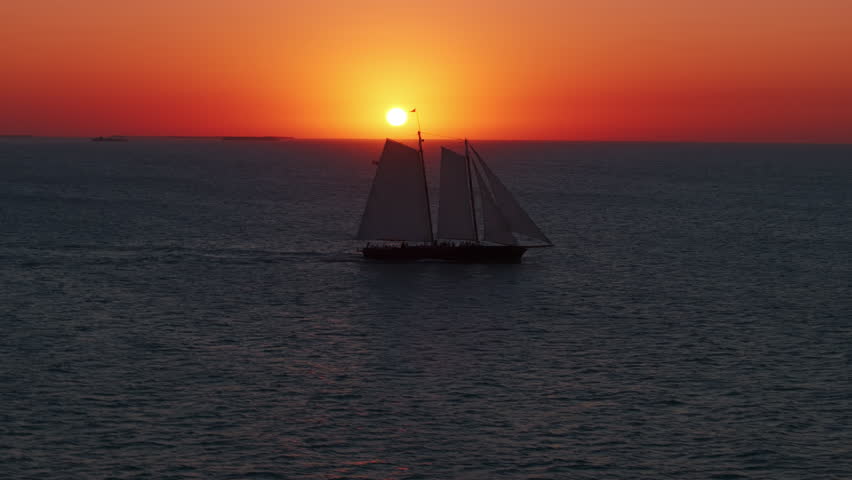 Enjoy a breathtaking aerial view of a stunning sailing ship gliding through sunset waters in Key West, Florida, with vibrant colors
