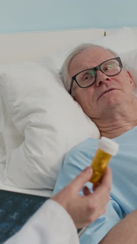 Vertical shot of doctor holding tablet with MRI scan prescribing pills to elderly patient in ward