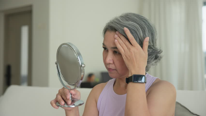 Asia adult people middle age old woman look at mirror dry skin face hand touch neck cheek stress sad at home elder health care aging beauty issue. Asian female aged eye botox filler plastic surgery.