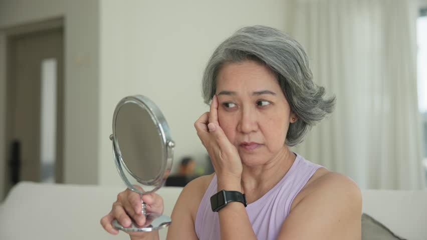 Asia adult people middle age old woman look at mirror dry skin face hand touch neck cheek stress sad at home elder health care aging beauty issue. Asian female aged eye botox filler plastic surgery.