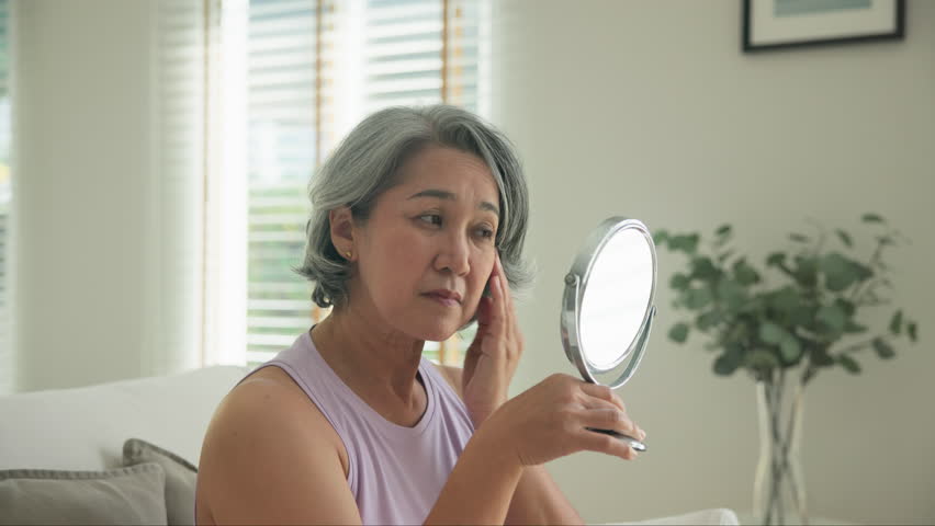 Asia adult people middle age old woman look at mirror dry skin face hand touch neck cheek stress sad at home elder health care aging beauty issue. Asian female aged eye botox filler plastic surgery.