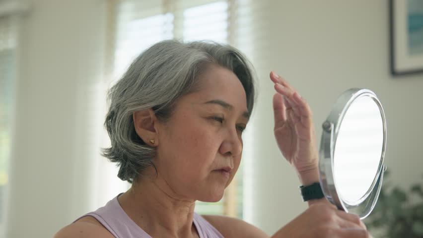 Asia adult people middle age old woman look at mirror dry skin face hand touch neck cheek stress sad at home elder health care aging beauty issue. Asian female aged eye botox filler plastic surgery.