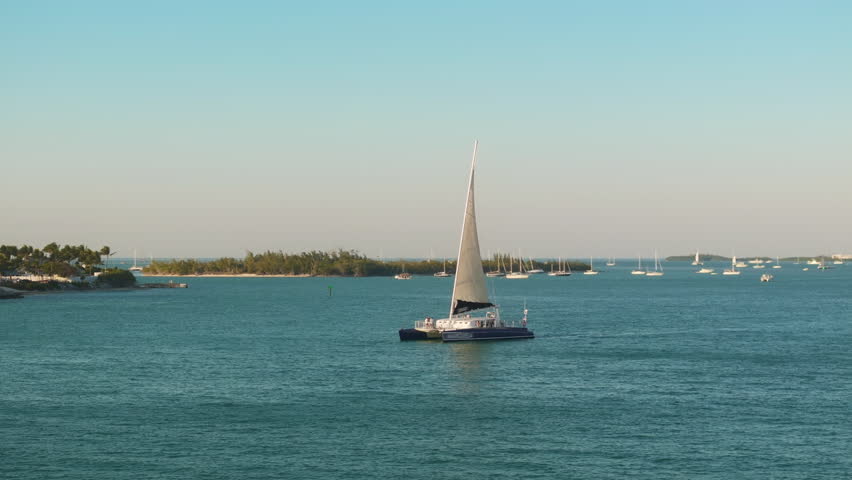 This aerial view of Sunset Key island in Key West, Florida highlights serene turquoise waters and a sailing boat, creating a picturesque scene of relaxation and tranquility