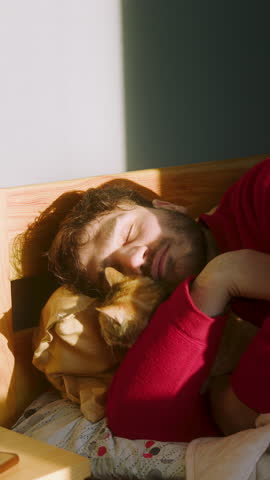 Man Sleeping in Bed While Cuddling His Cat in Warm Morning Sunlight – Cozy and Peaceful Moment of Pet Companionship and Relaxation ,vertical video