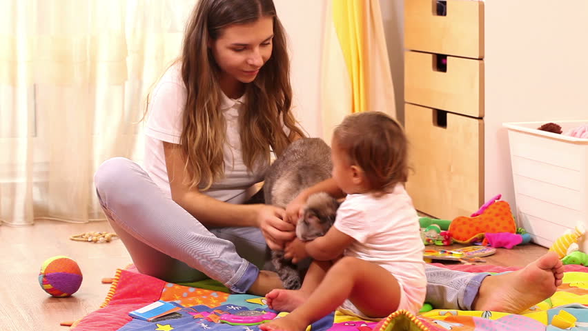 Beautiful mother and girl playing with cat at home