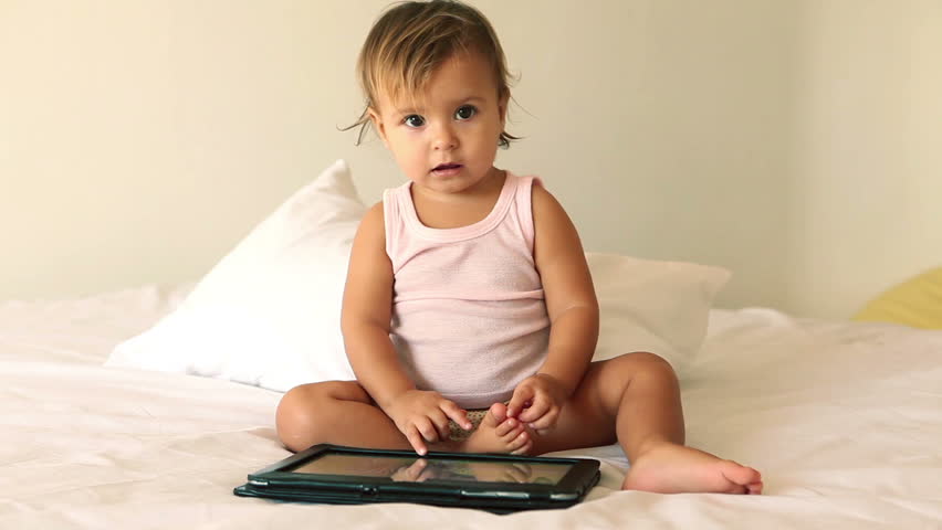Adorable little girl playing with digital tablet on bed