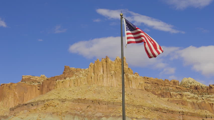 Medium shot of USA flag waving in the air during the day with blue sky in Cathedral Valley, Capitol Reef National Park, south-central Utah, USA