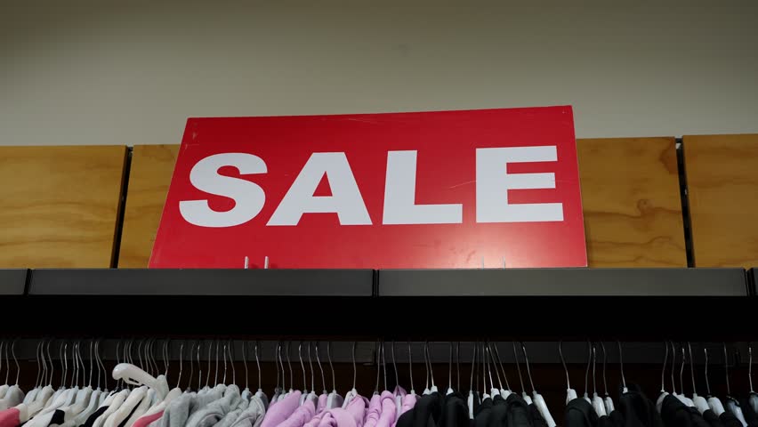 Red sale tag hanging in retail clothing store, close-up. Discounts and promotions in shopping malls, seasonal clothing sales. Black Friday
