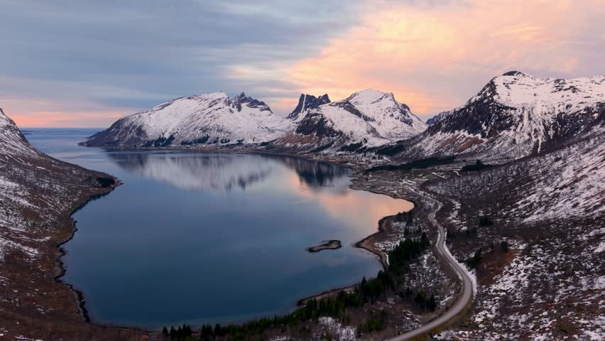 Breathtaking aerial view of a fjord in Senja, Norway, with snow-capped mountains at sunset