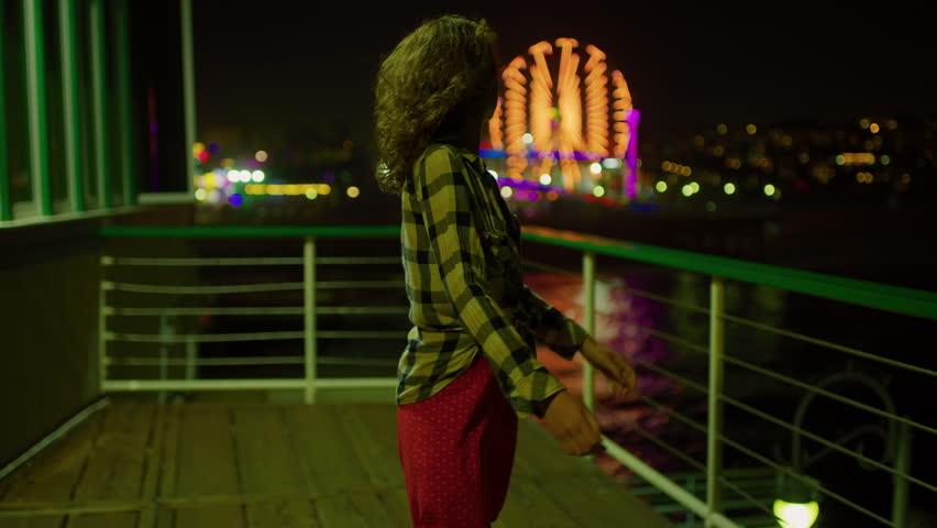 A girl enjoying a night walk on Santa Monica pier with ferris wheel lights, California, USA.