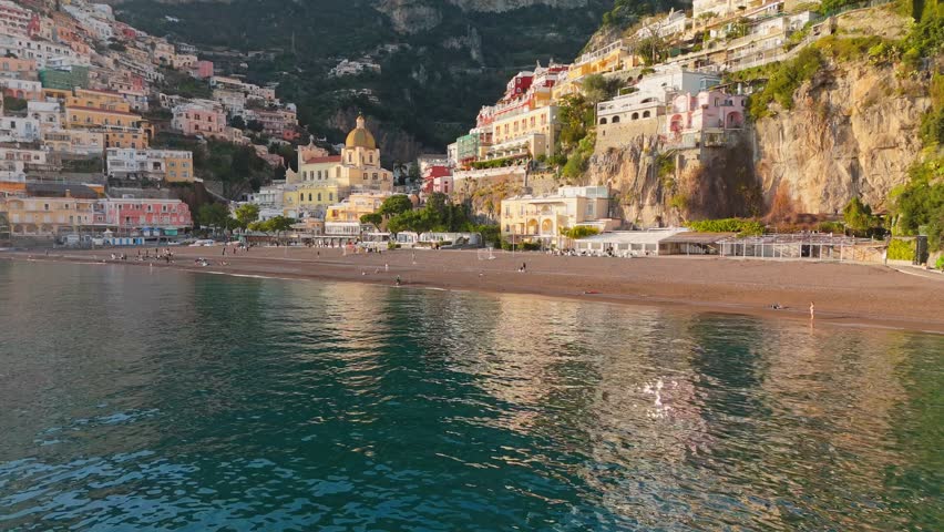 Epic shot of colorful village Positano, Amalfi coast, Italy. Fly over the sea near colorful houses, church and beach in Positano at sunset