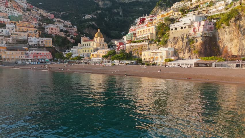 Epic shot of colorful village Positano, Amalfi coast, Italy. Fly over the sea near colorful houses, church and beach in Positano at sunset