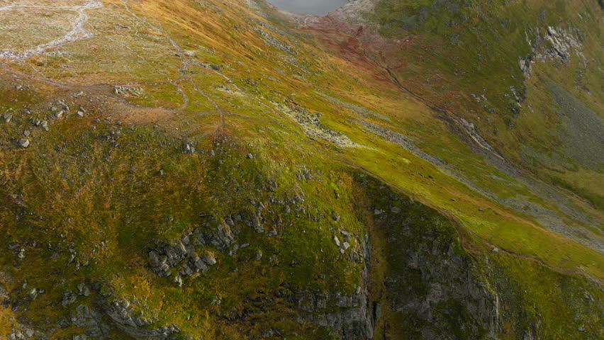 A tranquil aerial dolly over lush green yellow hills to Forsvatnet Pond above Kvalvika Beach, Ryten in Lofoten, Norway