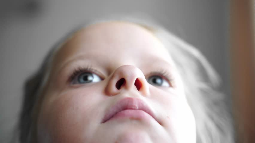 Girl inflates and deflates nostrils while moving nose. Close-up of face from a low angle. Expressive look with wide-open blue eyes. Detailed nostrils and fair skin. Macro shot. Candid subtle motion