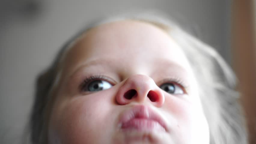 Girl inflates and deflates nostrils while moving nose. Close-up of face from a low angle. Expressive look with wide-open blue eyes. Detailed nostrils and fair skin. Macro shot. Candid subtle motion