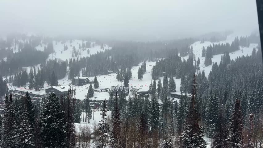 Extreme wide landscape shot POV from a ski lift of the ski lodges at the Brighton Ski Resort in Utah, USA surrounded by snow covered pine trees during a winter snowstorm