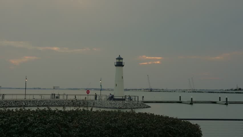 A tranquil view of a lighthouse from a Dallas, Texas at dusk. The calm water, cloudy sky, and distant shoreline create a peaceful and scenic landscape.