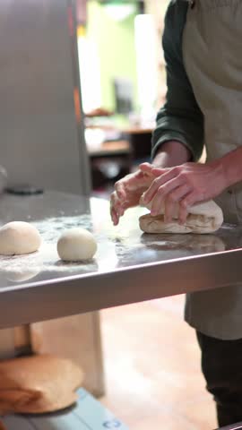 Professional baker carefully kneading bread dough on metal surface, showcasing traditional artisan baking skills and manual food preparation technique