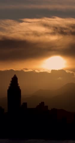 Portrait footage of the sun setting in the evening over the old town of Benidorm in Spain showing the beautiful yellow sun set with clouds in the sky along side high rise apartments building