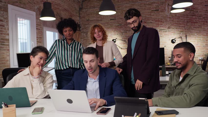 Diverse team collaborating on a project, using a laptop in a modern office environment. Slow motion emphasizes their teamwork and focused expressions