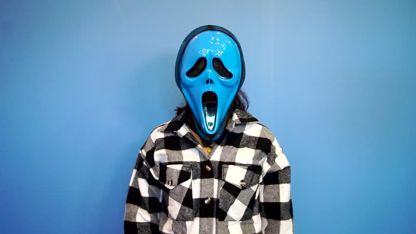 A girl in a blue color ghost mask giving listening secret talk gesture on a blue color background.