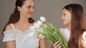 A mother and her young daughter smile and connect as they hold a bouquet of white tulips. The cozy indoor setting creates a warm atmosphere full of affection and joy between them - Powered by Shutterstock - Get 15% off with code: PIKWIZARD15