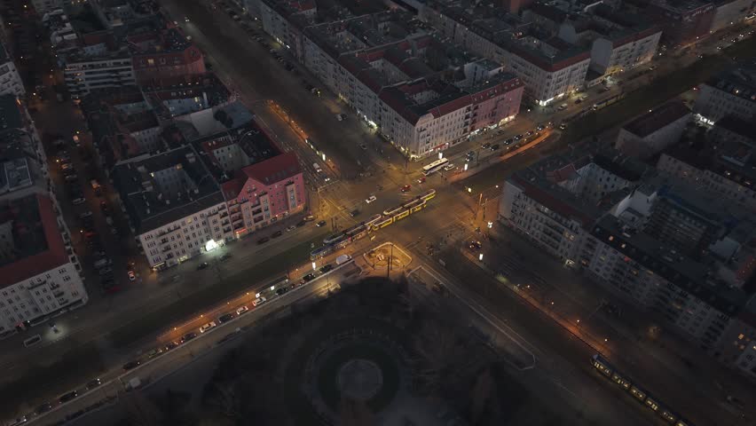 Aerial 4K drone footage of a busy city intersection in Berlin, Germany, at dusk. Featuring trams, moving cars, and illuminated streets. 
