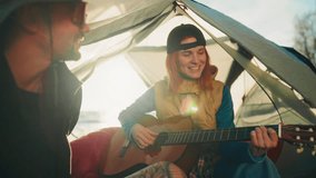 Two campers relaxing in tent on seacoast in summer, playing guitar, tourism. Happy man and woman enjoying solitude in nature and music, loving couple spending weekend together in travel, slow motion - Powered by Shutterstock - Get 15% off with code: PIKWIZARD15