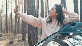 Young woman riding outside car in forest and recording video using smartphone. Blogger creating video content. Moving hand with phone in it and pose with smile. - Powered by Shutterstock - Get 15% off with code: PIKWIZARD15