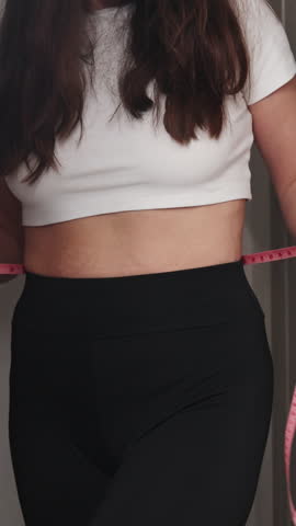 woman measuring waist with centimeter and walks on body composition scale. female want to loose weight,get slim.girl with visceral fat on belly.fitness concept.