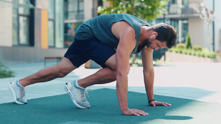 Young man exercising outside. Video process of guy doing mountain climber exercise. Running fast in horizontal position on the same place. Training near urban view.