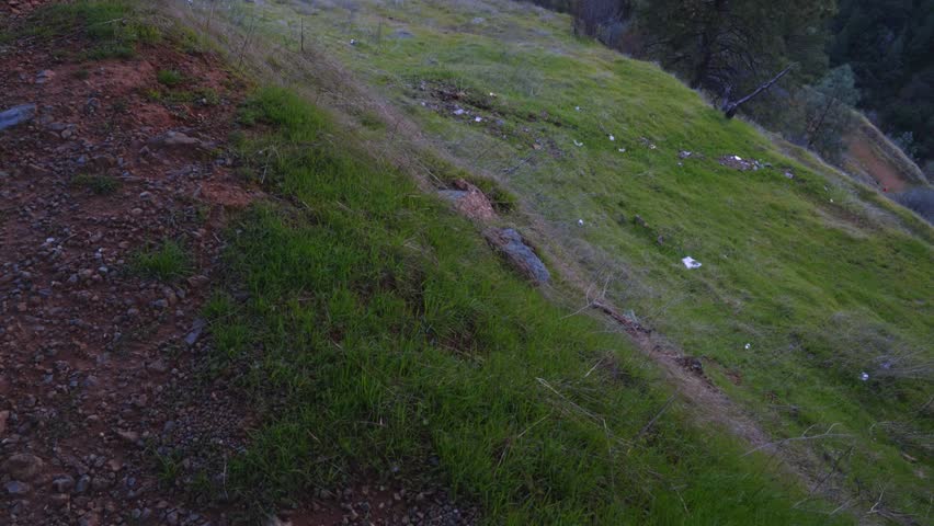The camera tilts upward, gradually revealing a panoramic view of the mountain landscape. The frame features green hills, a winding river, and a bridge connecting the shores in California