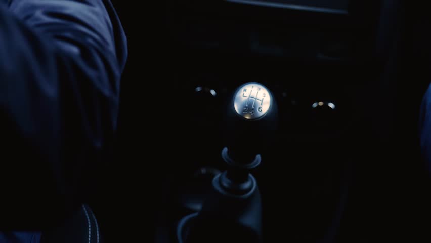 Young man inside car. Close up of guy driving and hold hand on transmission. Using it from time to time. Experienced driver. Slow motion.