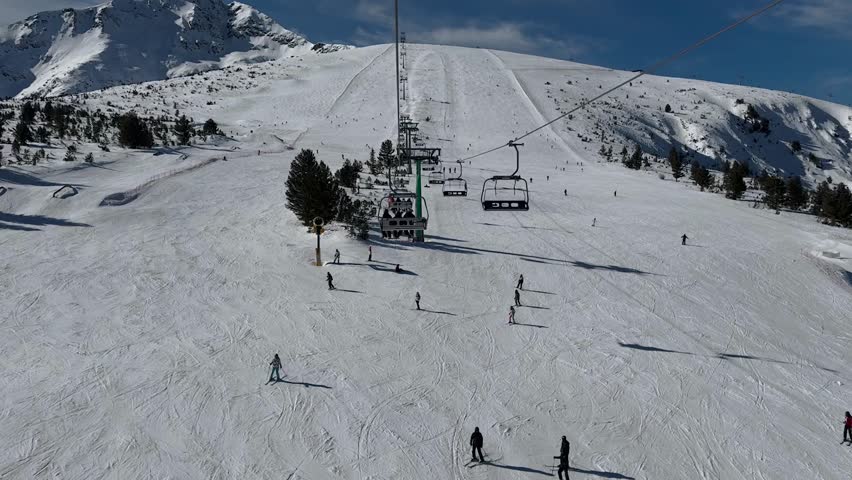 Aerial view over snowy mountain winter forest with chair lift at ski resort. Ski lift cable car top down drone shot. Winter landscape scene with snow covered trees. Outdoor tourism skiing snowboarding