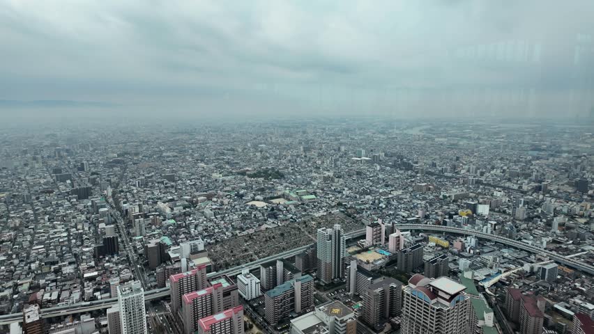 Overlooking Osaka cityscape with buildings, roads, and urban development under a cloudy sky