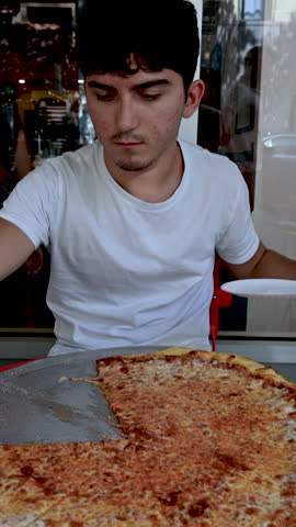 New York, USA, August 19, 2024. A young Caucasian man enjoys a large slice of American pizza. Lifestyle eating local food. Vertical format.