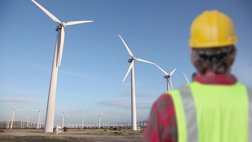 4k Contractor Inspector Wearing Hard Hat Looks On As Alternative Energy Wind Turbines Generate Clean Energy in the Desert of California.