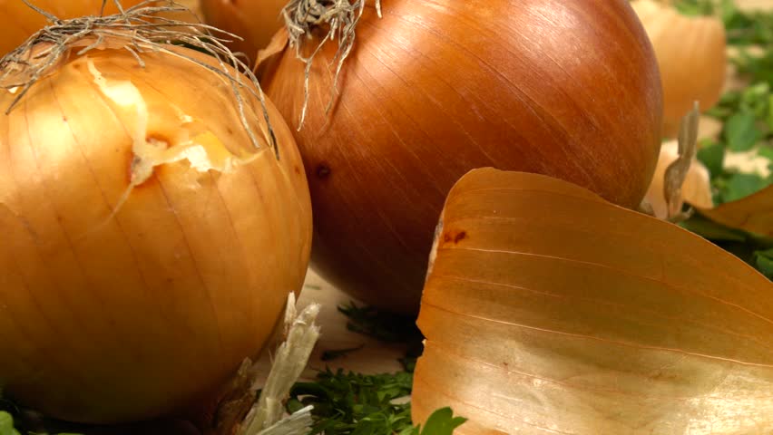Bulbs of yellow onion and their peels lie on a chopped dill and parsley on a board