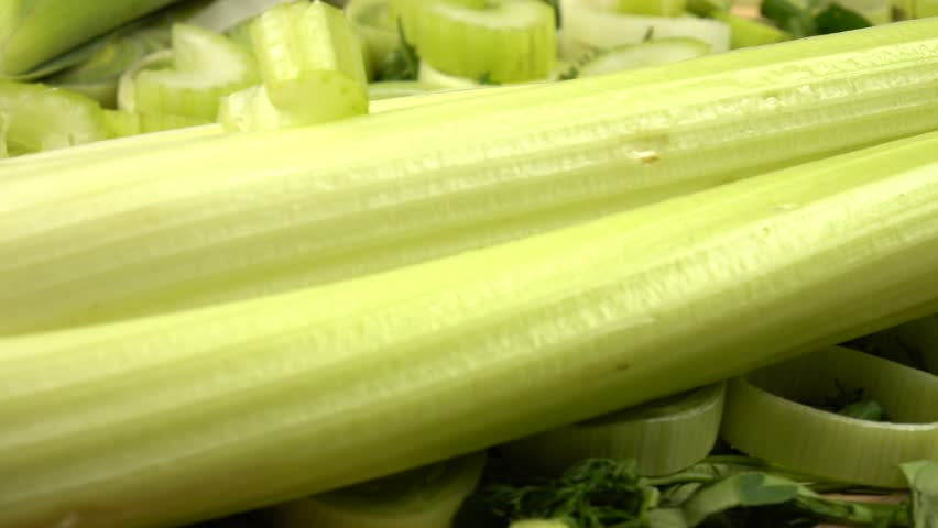 Whole and cut, peeled and unpeeled leek and celery lie on a chopped dill and parsley