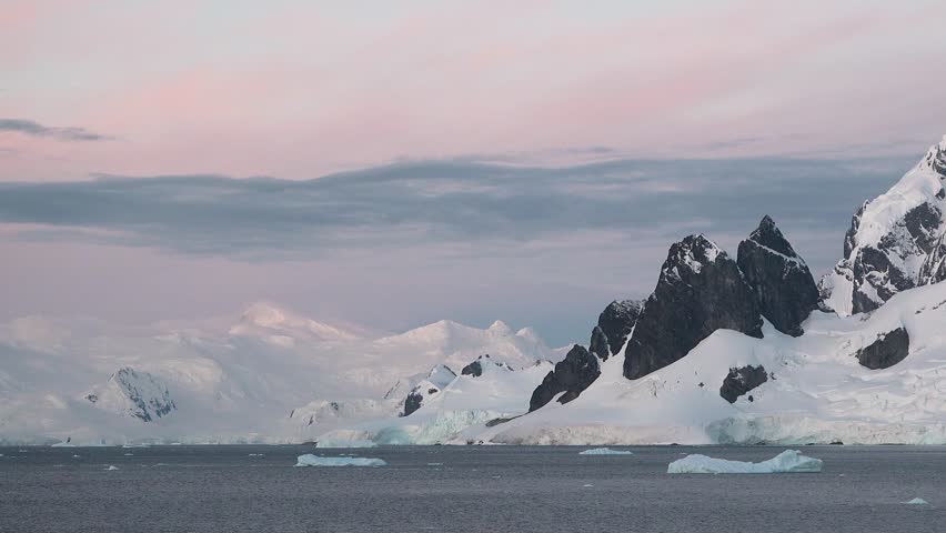 View the breathtaking twilight in Antarctica featuring majestic mountains and drifting icebergs surrounded by a serene ocean. The colors of the sky create a magical atmosphere.