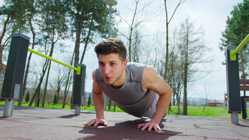 Young guy doing push-ups outdoors in a park setting.