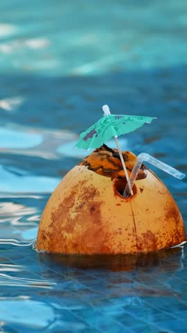 Fresh Coconut juice cocktail with drinking straw floating in a refreshing blue swimming pool.