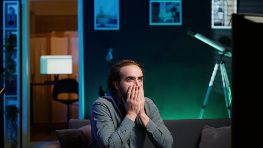 Furious sports fan in disbelief during match broadcast after own team fails to score, expressing anger. Enraged man acting childish in frustration after seeing favorite club commit blunder, camera A