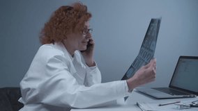Happy adult woman doctor radiologist discussing CT scan of patient's lungs with colleagues by phone in hospital office. Pulmonologist examines MRI or pulmonography and uses a cell phone. Chest x-ray. - Powered by Shutterstock - Get 15% off with code: PIKWIZARD15