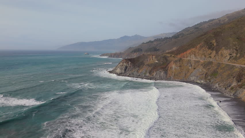 Experience the beauty of Big Sur, California, with an aerial view along Highway 1, where a car navigates stunning scenery of crashing waves and towering cliffs showcasing natures grandeur