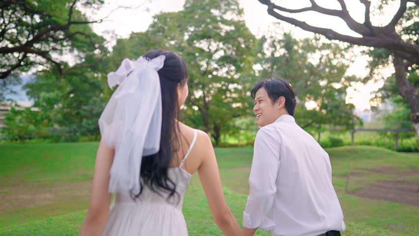 Asian young married couple holding hand each other in park during sunset. Attractive romantic groom and bride celebrating their love and Valentine