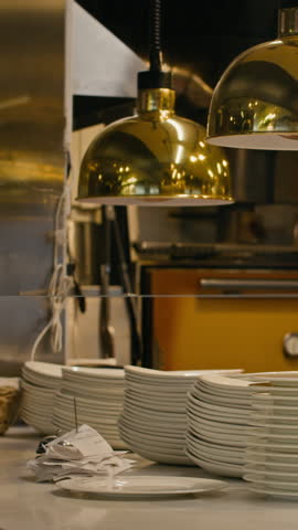 Vertical shot of restaurant kitchen with white plates, golden lights, and kitchen tools